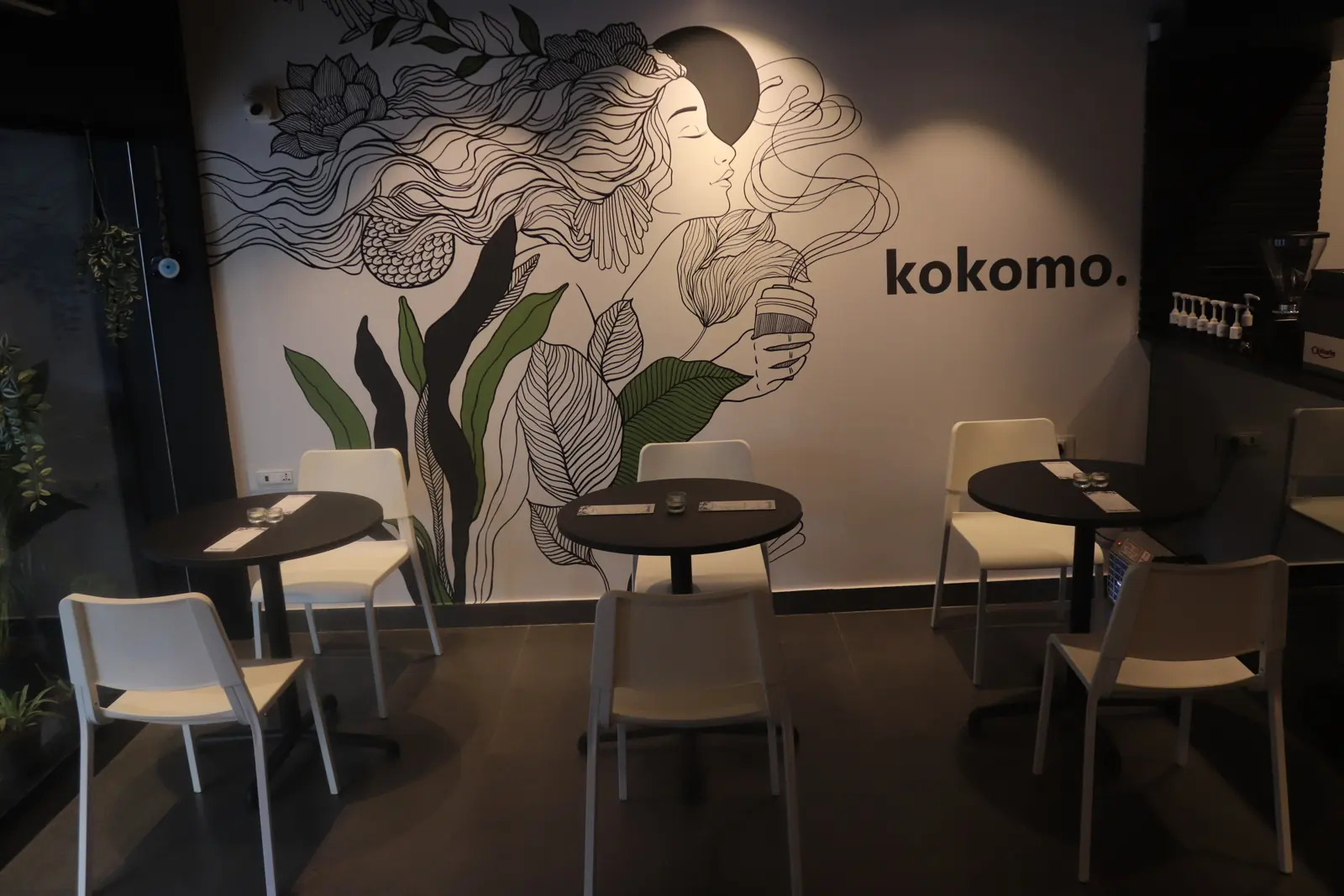 The black-and-white line-art mural with the kokomo name, above round black tables and white chairs